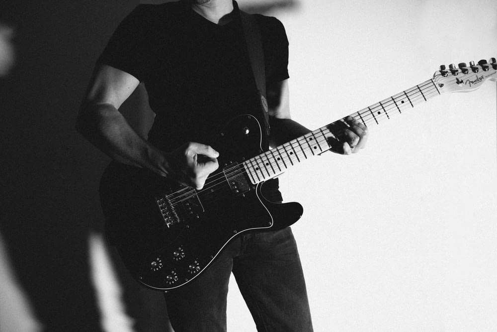 grayscale photography of man standing while playing guitar
