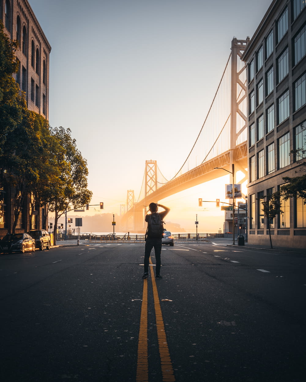 man takes photo of suspension bridge at the city during daytime
