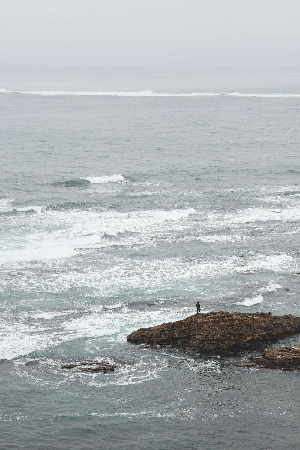 Persona parada en una formación rocosa cerca de la orilla del mar