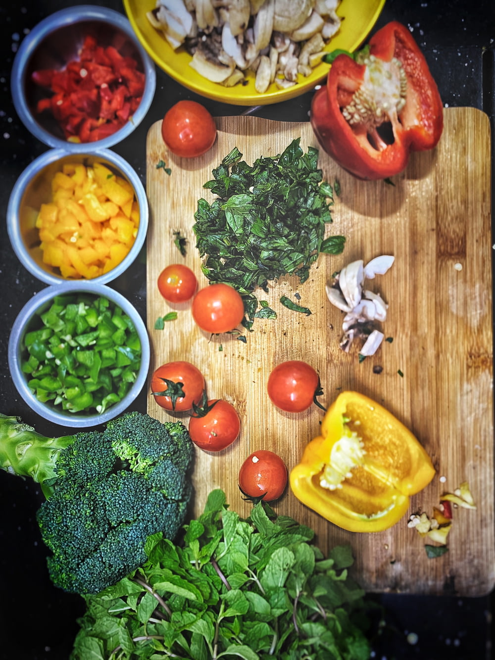 orange tomatoes near sliced yellow bell pepper, broccoli on wooden chopping board