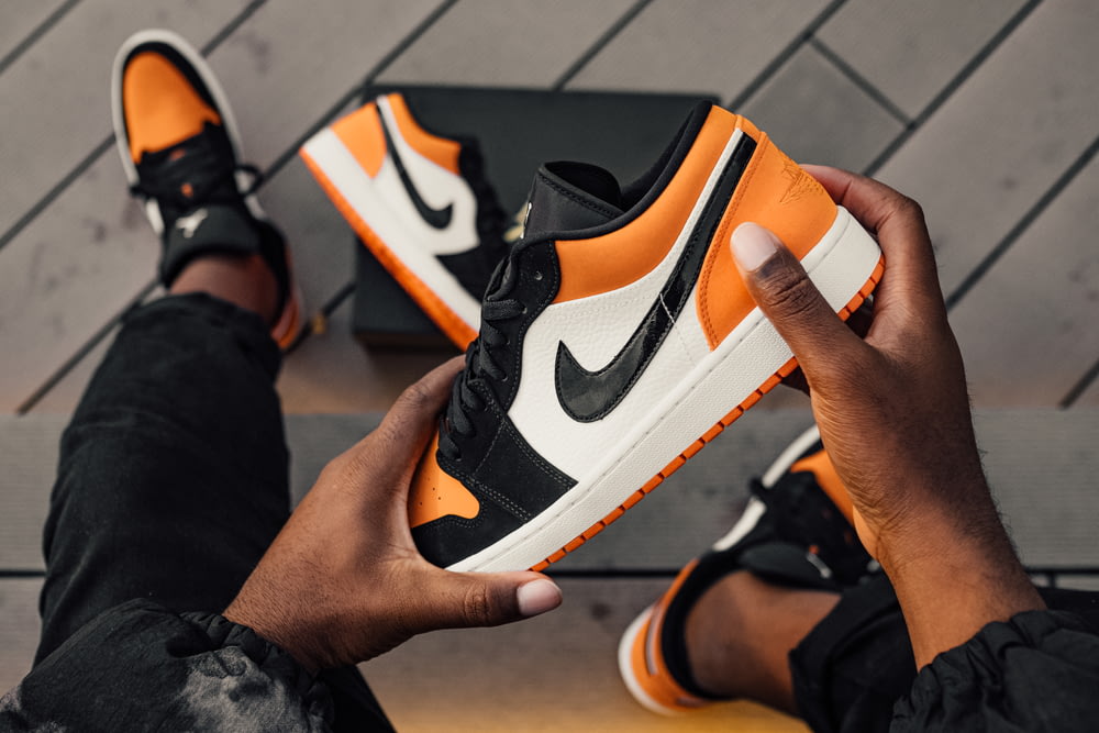 persona seduta e in possesso di scarpe da ginnastica basse Nike SB arancione-bianco e nero