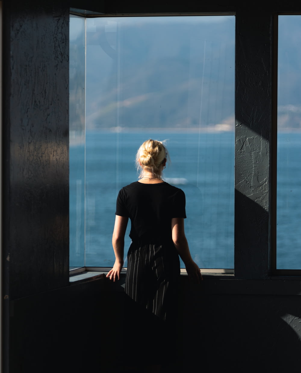 person wearing black t-shirt standing near glass window while facing on body of water