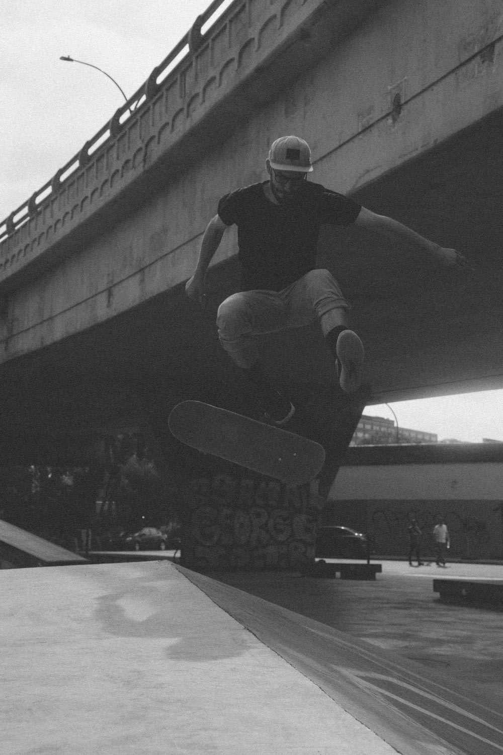 greyscale photograph of man doing tricks while riding skateboard