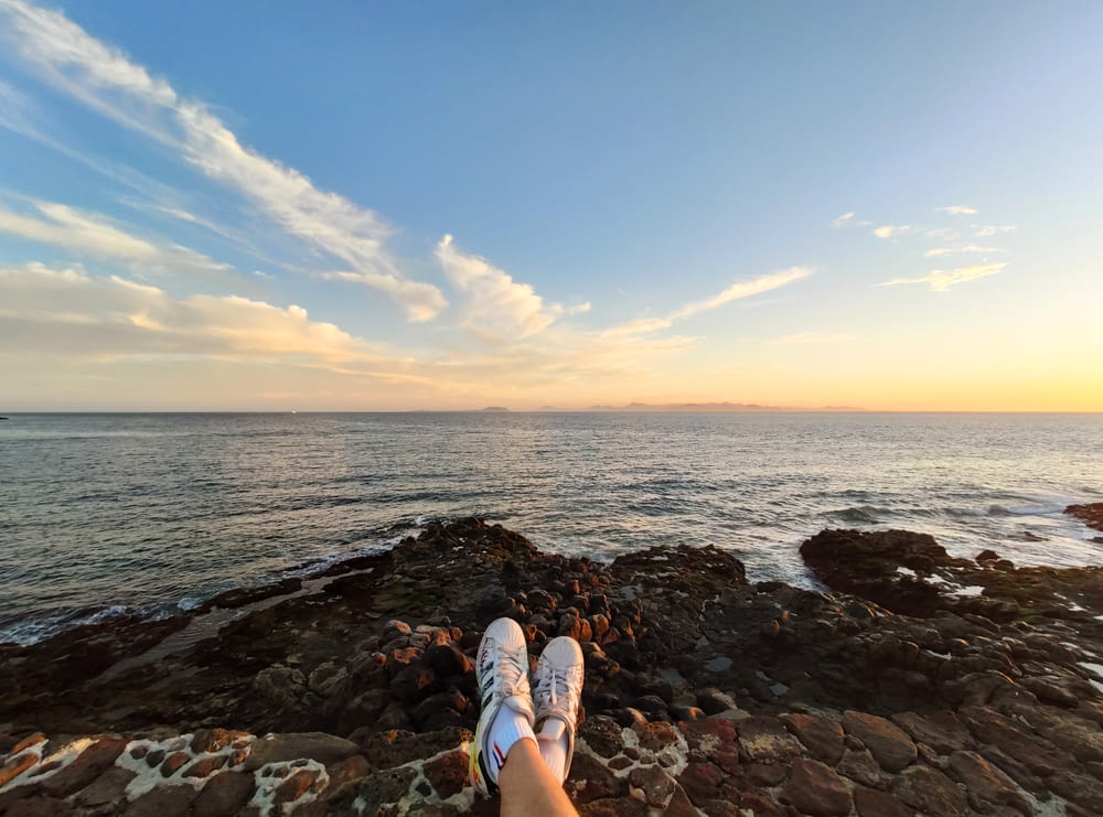 person in blue and white sneakers sitting on rocky shore during daytime