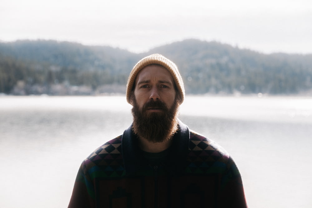 Un uomo con la barba in piedi di fronte a un lago