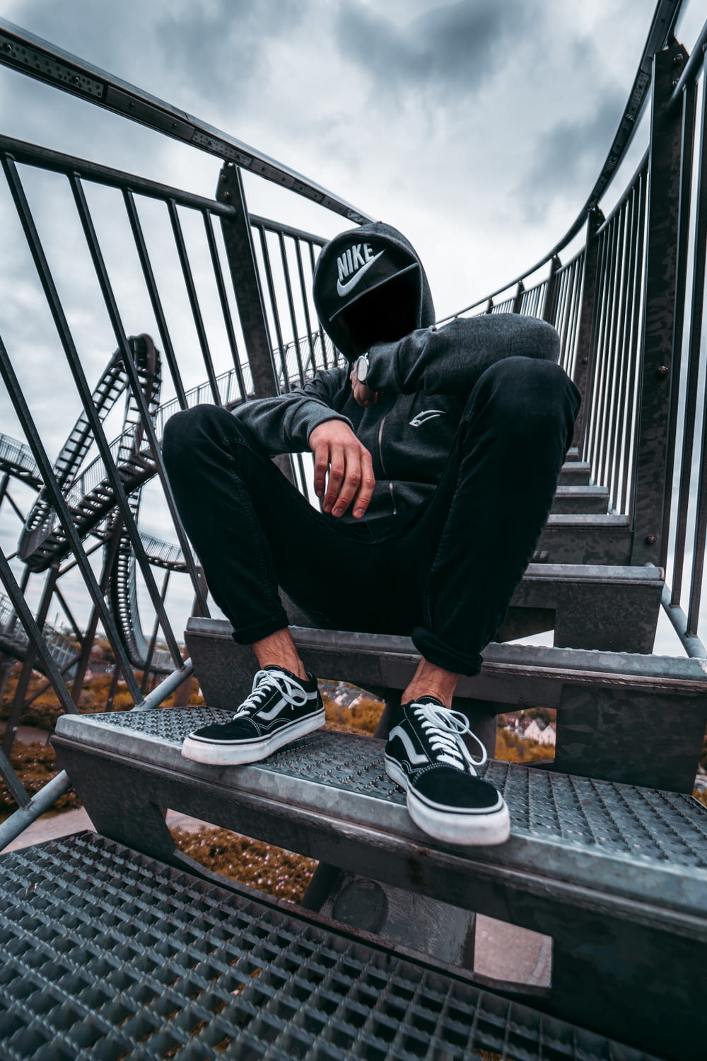 man in black pants and black and white nike sneakers sitting on black metal railings