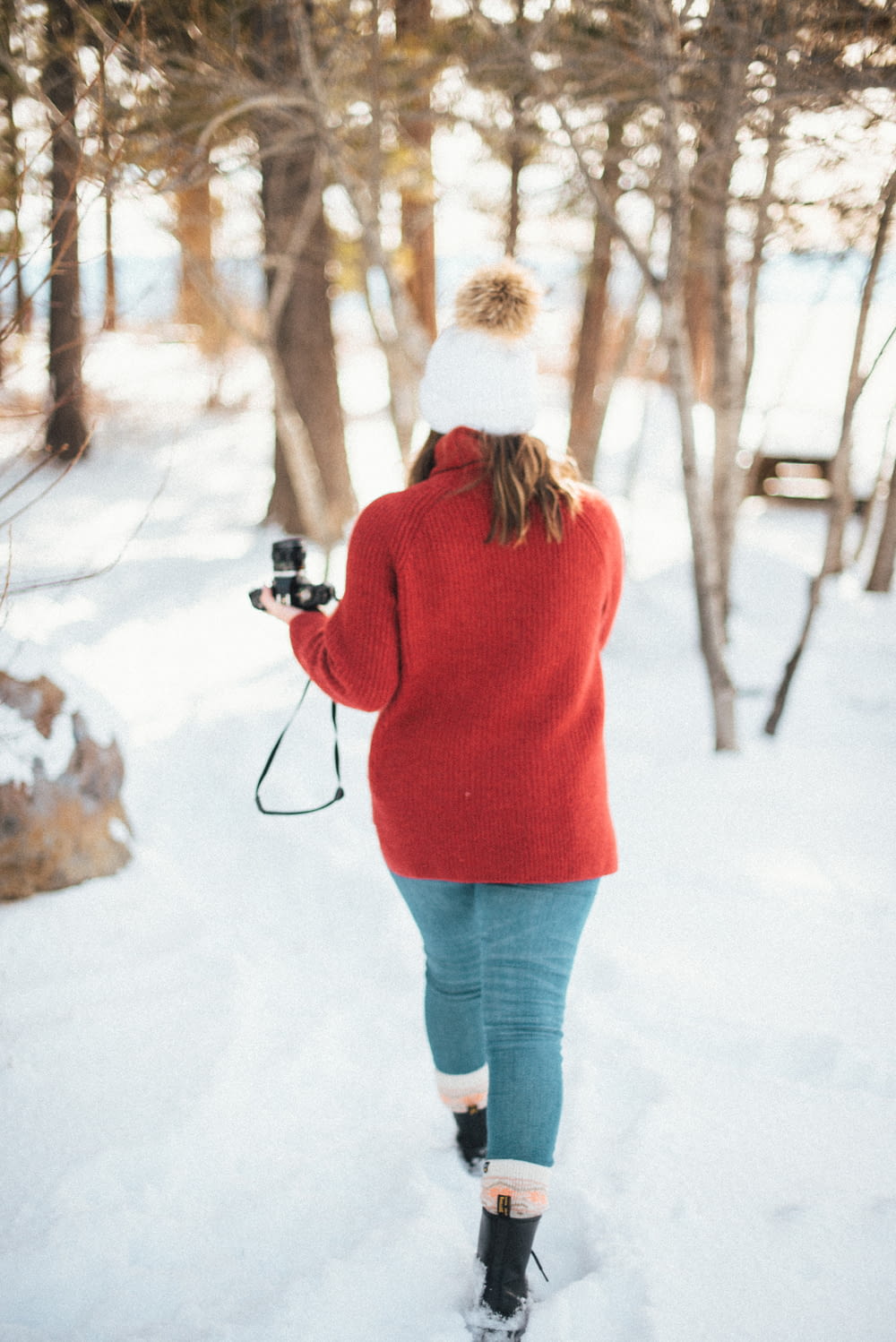 woman in red sweater and blue denim jeans holding camera on snow covered ground during daytime