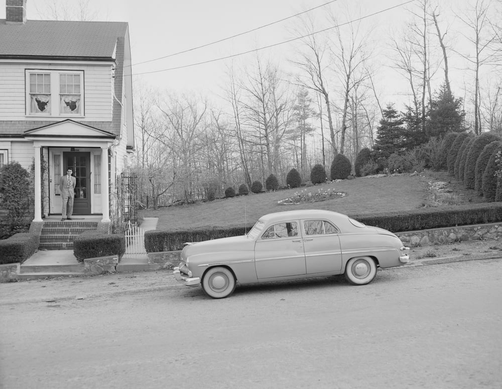 Foto en escala de grises de un coche antiguo aparcado al lado de la casa