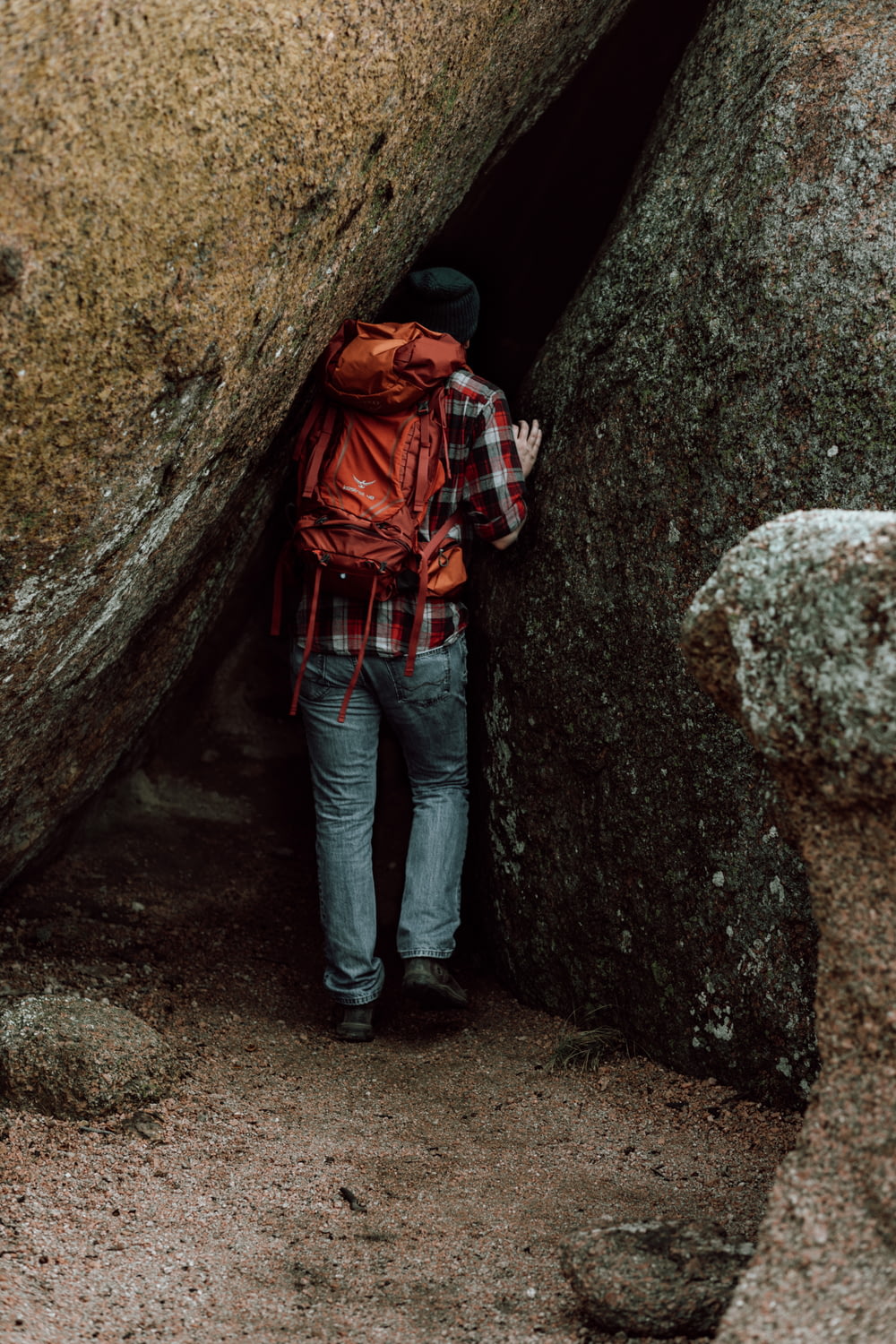 woman in red and black plaid hoodie and blue denim jeans standing beside brown rock formation