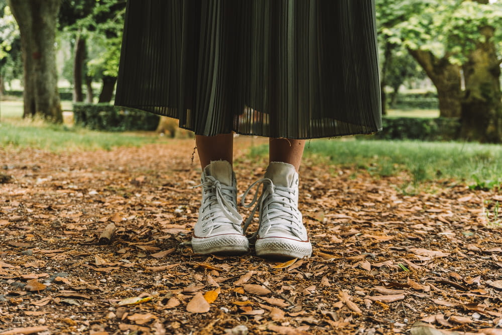 person in black skirt and white sneakers standing on brown dried leaves during daytime