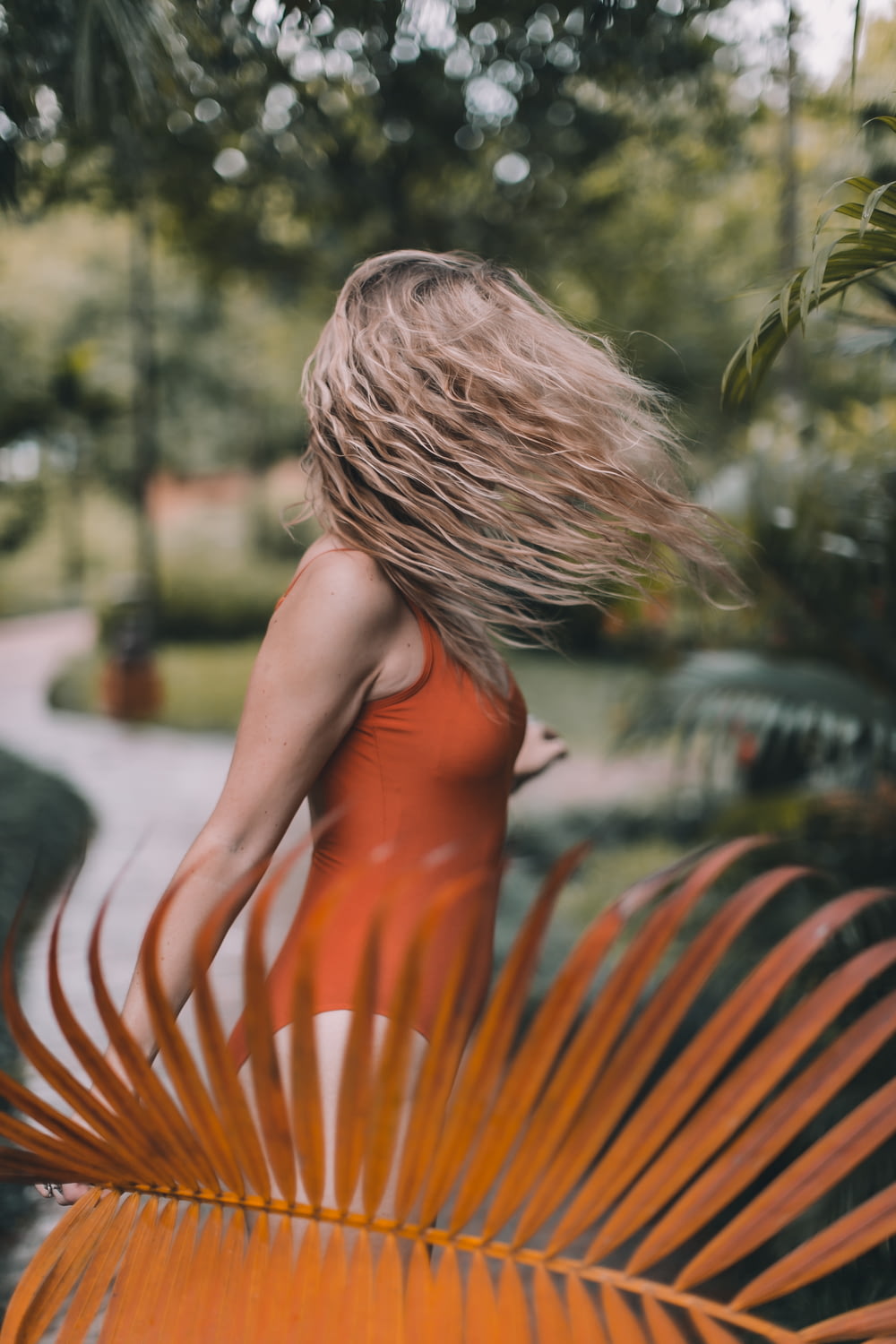 woman in orange halter top standing near green trees during daytime