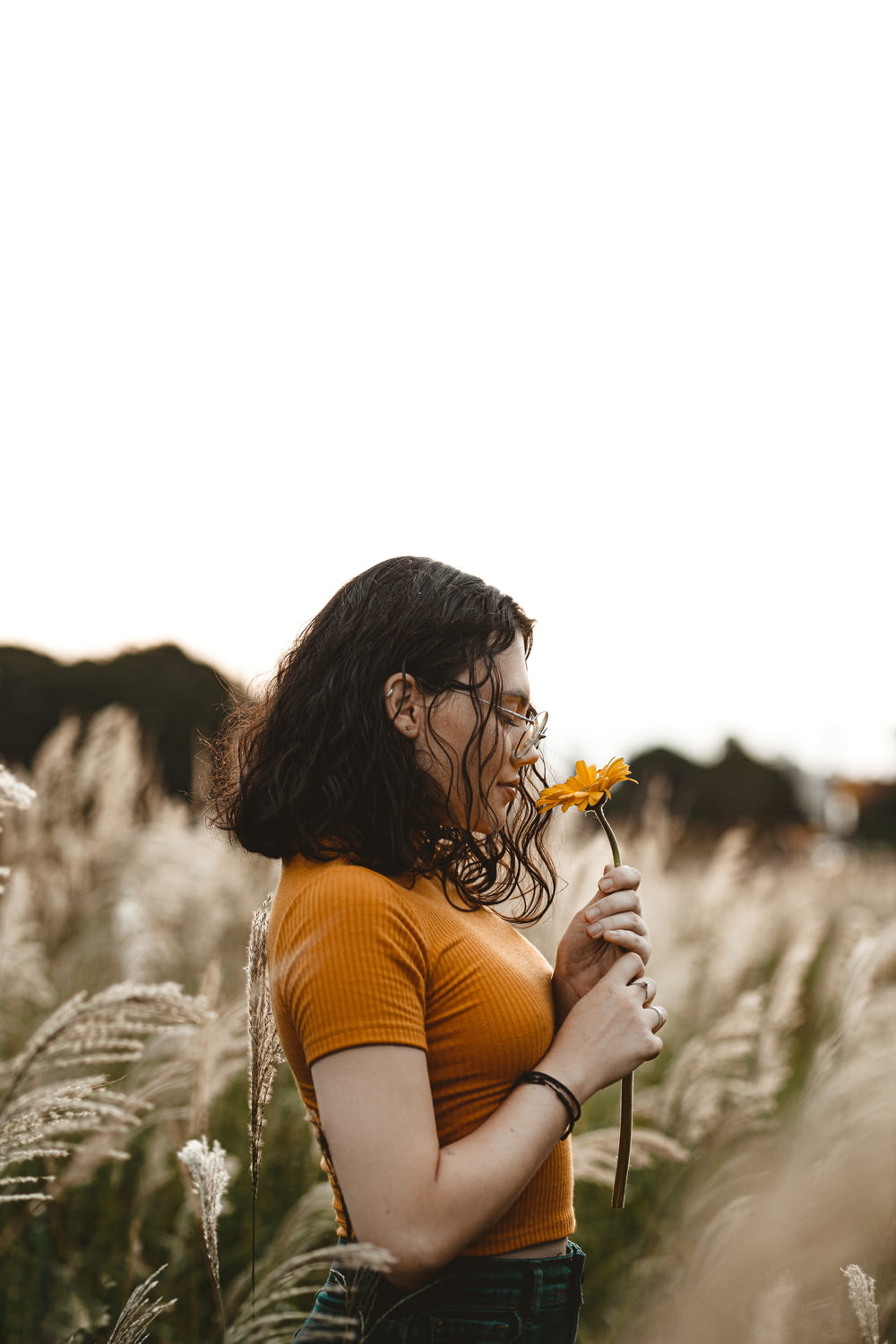 mujer en camiseta sin mangas naranja sosteniendo flor amarilla durante el día