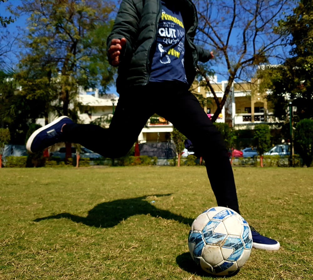 Hombre con camisa de manga larga adidas azul y blanco y pantalones negros jugando al fútbol durante el día