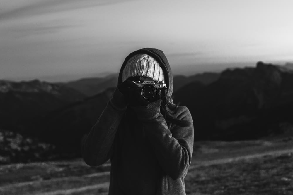 grayscale photo of woman in black jacket holding camera