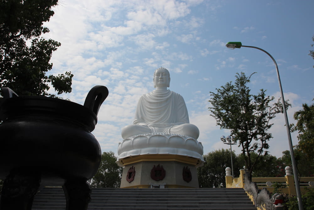 white concrete buddha statue near green trees during daytime