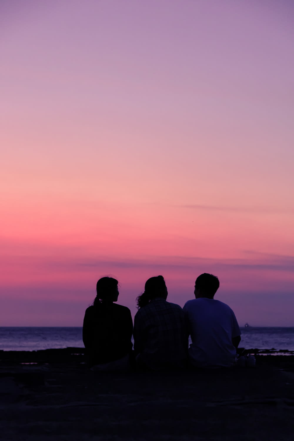 Silhouette von 2 Männern und Frauen, die während des Sonnenuntergangs am Meeresufer sitzen