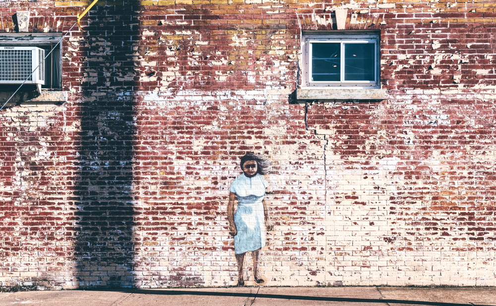 girl in white dress standing beside brown brick wall during daytime