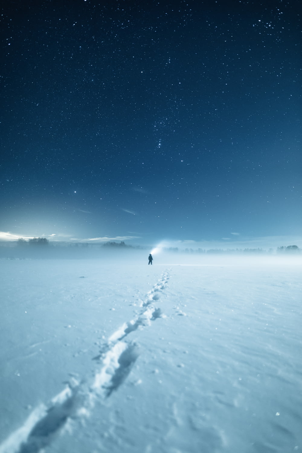 Persona con chaqueta negra caminando sobre suelo cubierto de nieve durante el día