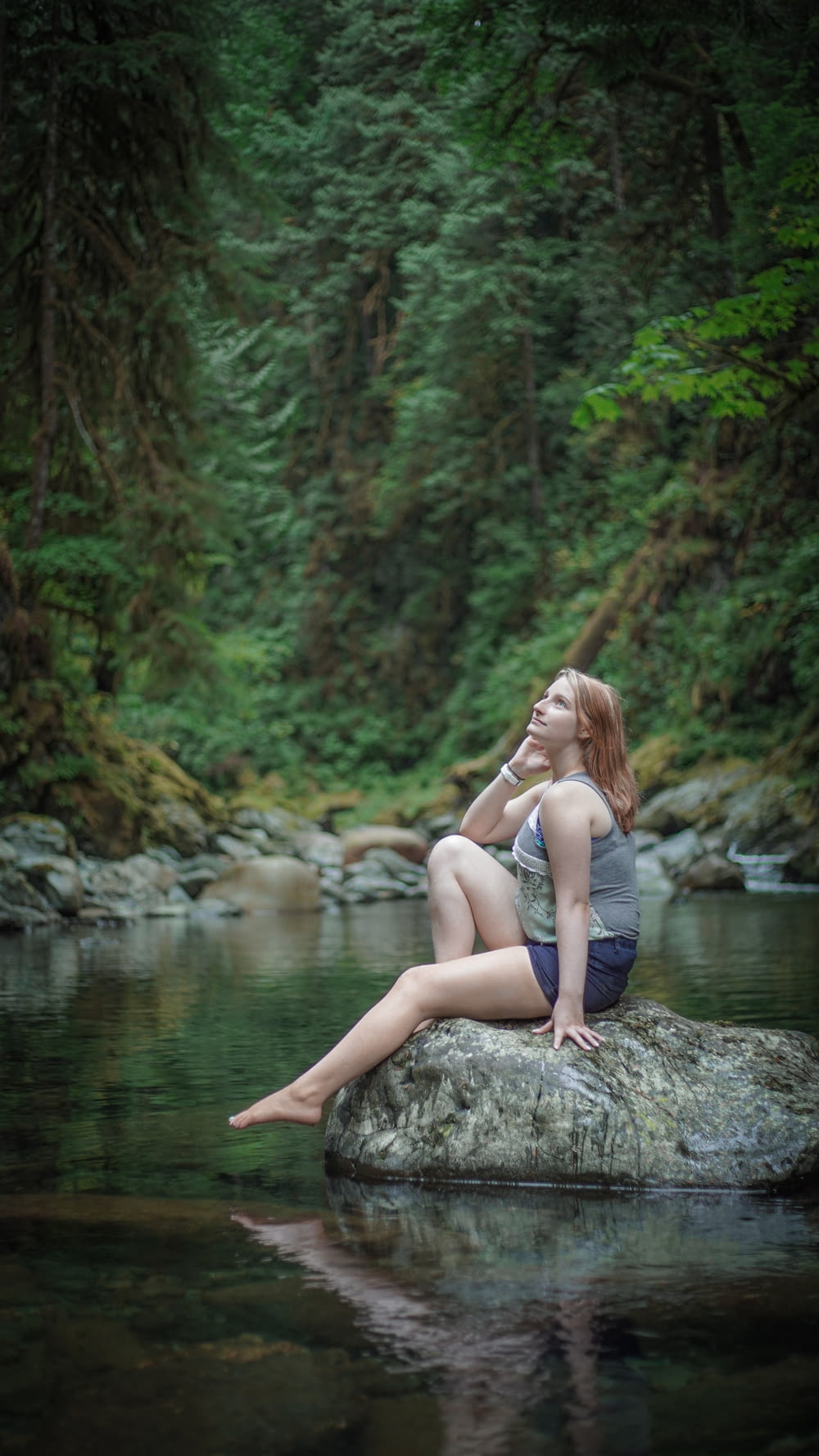 woman in white tank top sitting on rock near river during daytime