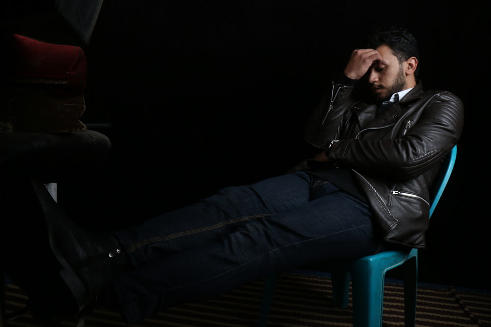 Mann in schwarzer Lederjacke sitzt auf blauem Plastikstuhl