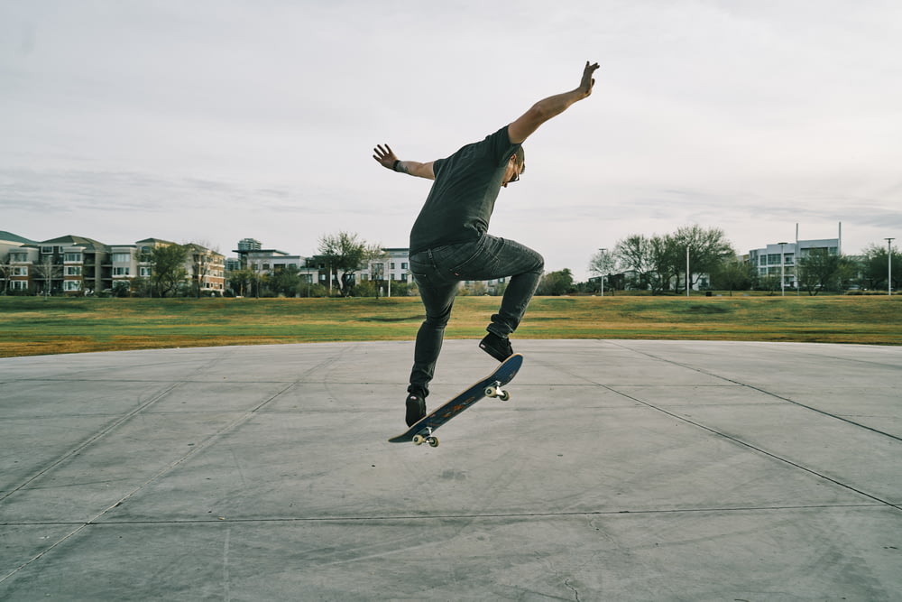 Uomo in t-shirt nera e jeans blu in denim che cavalca lo skateboard durante il giorno