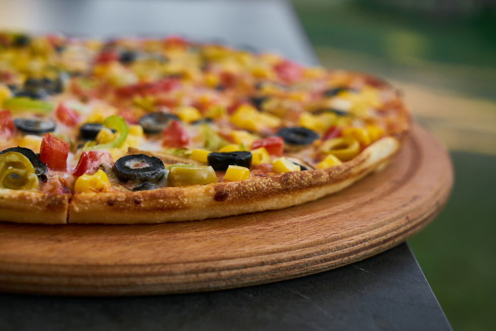 pizza with green and red berries and black berries on brown wooden round plate