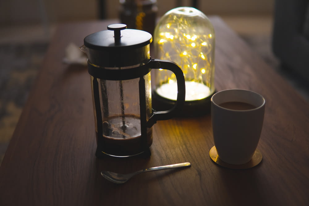 white ceramic mug beside black coffee press on brown wooden table