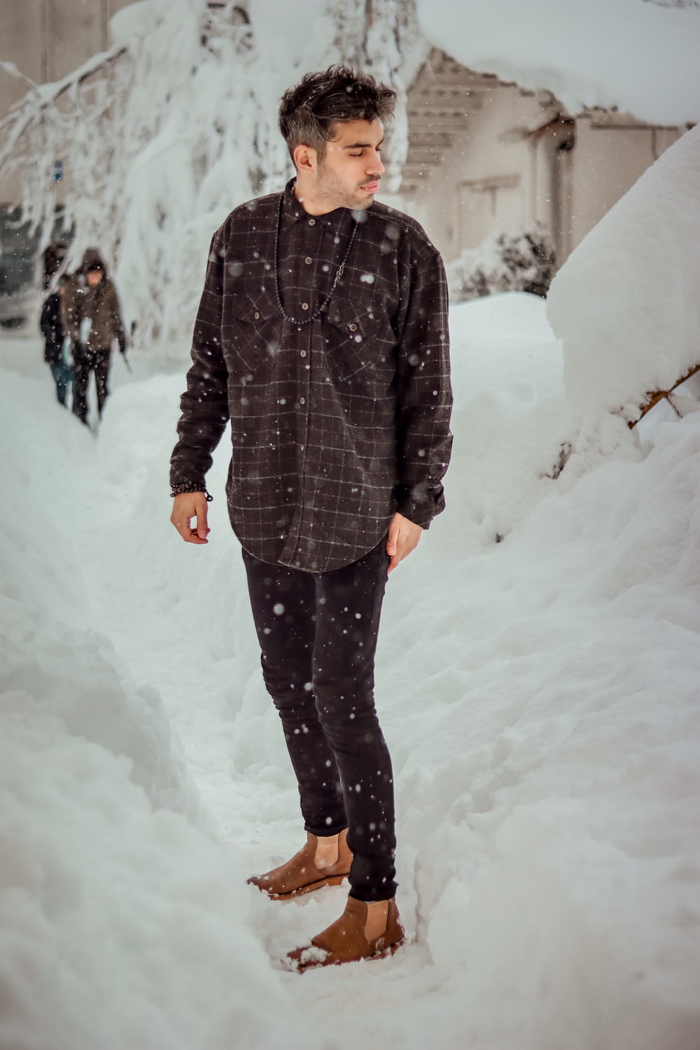 homem em casaco listrado preto e cinza em pé no chão coberto de neve durante o dia