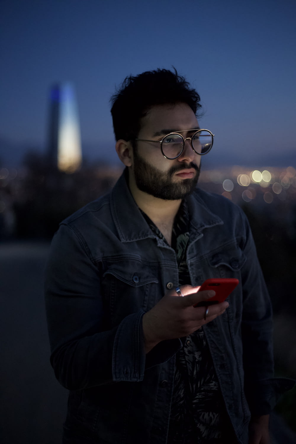 homme en veste en cuir noir tenant un smartphone rouge pendant la nuit