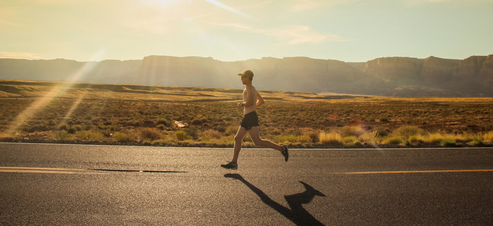 hombre en pantalones cortos negros corriendo en carretera de asfalto gris durante el día