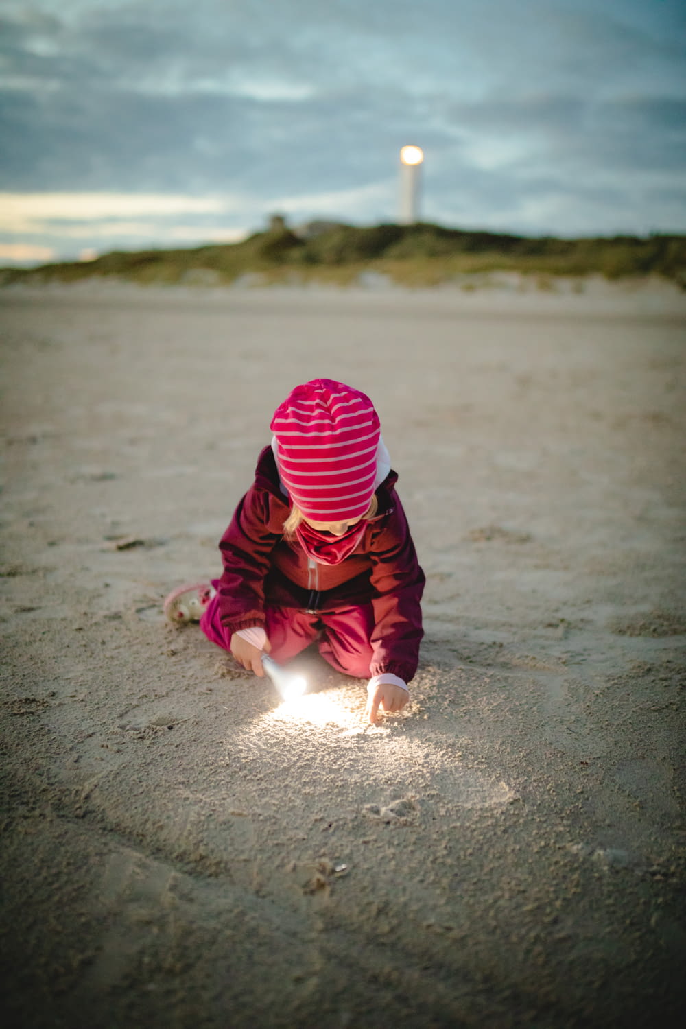 child in red and black hoodie playing on beach shore during daytime