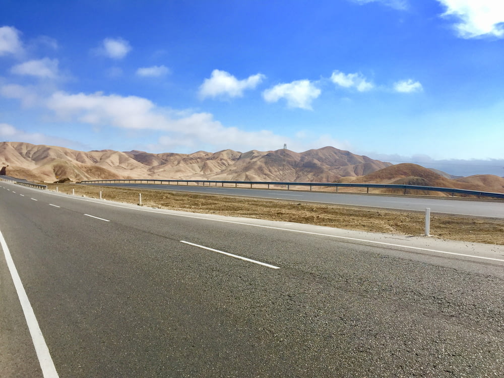 estrada de concreto cinza perto da montanha marrom sob o céu azul durante o dia