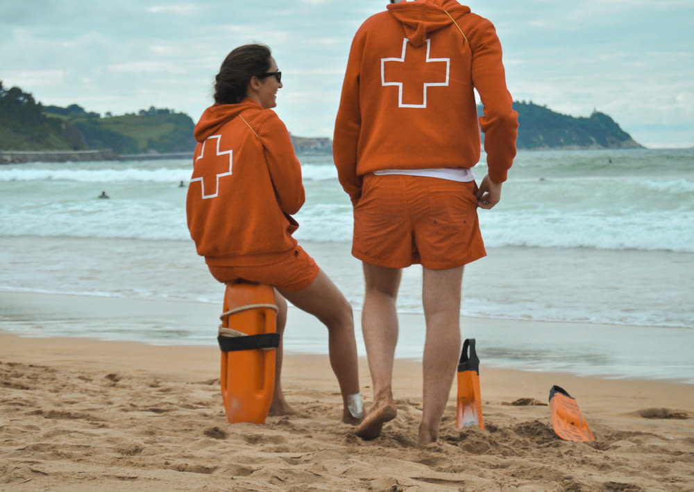 uomo in felpa con cappuccio arancione in piedi sulla spiaggia durante il giorno