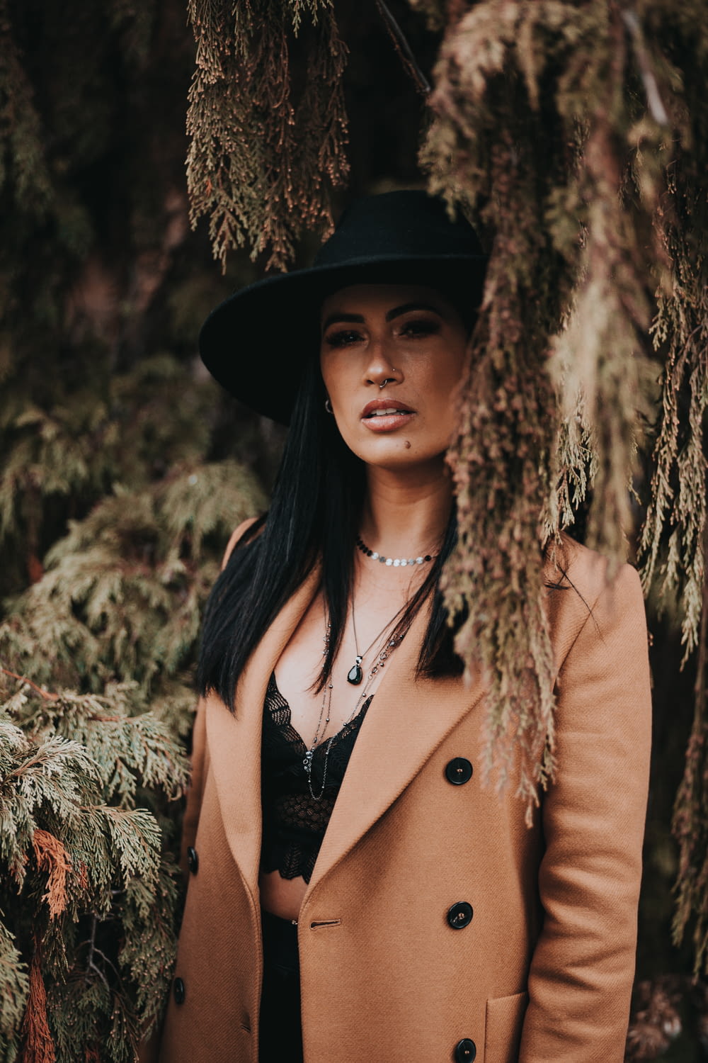woman in brown coat and black hat standing near brown tree during daytime