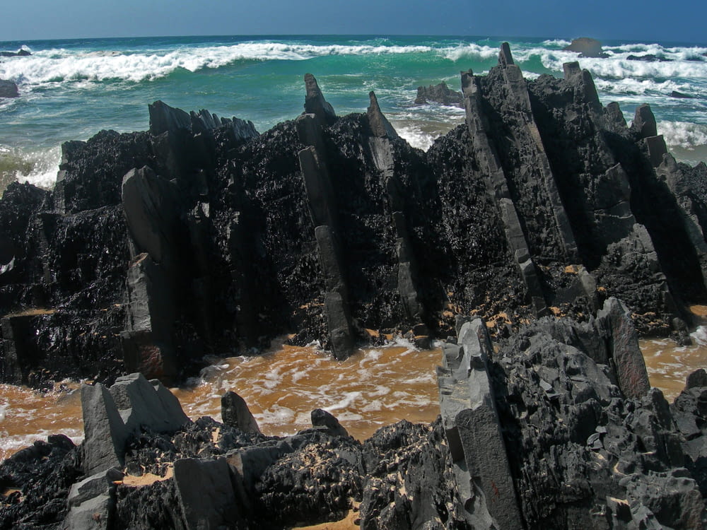 formação rochosa negra perto do corpo de água durante o dia
