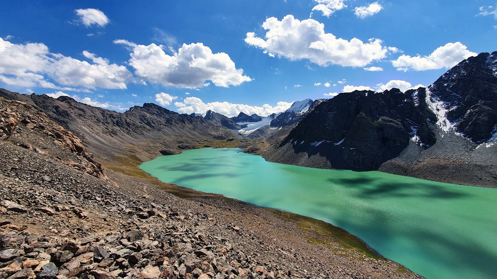 lake in the middle of mountains under blue sky and white clouds during daytime
