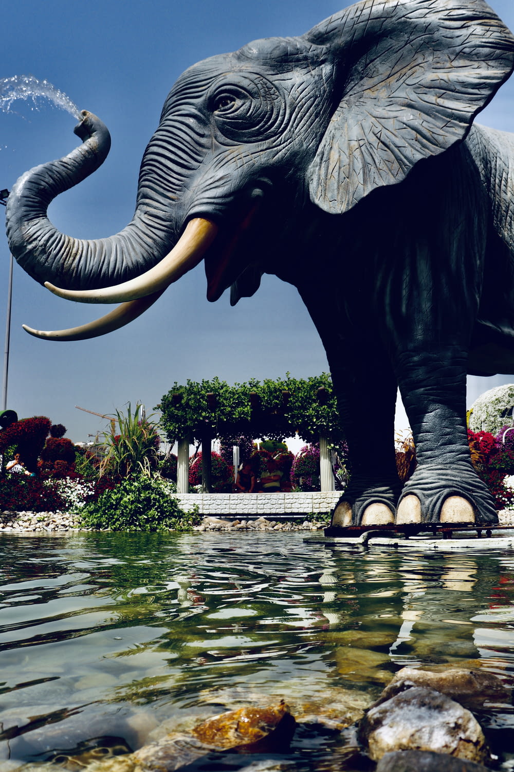 elephant statue on water near flowers and trees during daytime