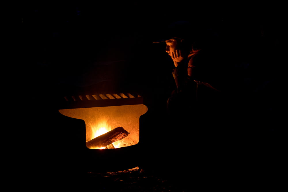 silhueta do homem que usa o chapéu em pé perto da fogueira