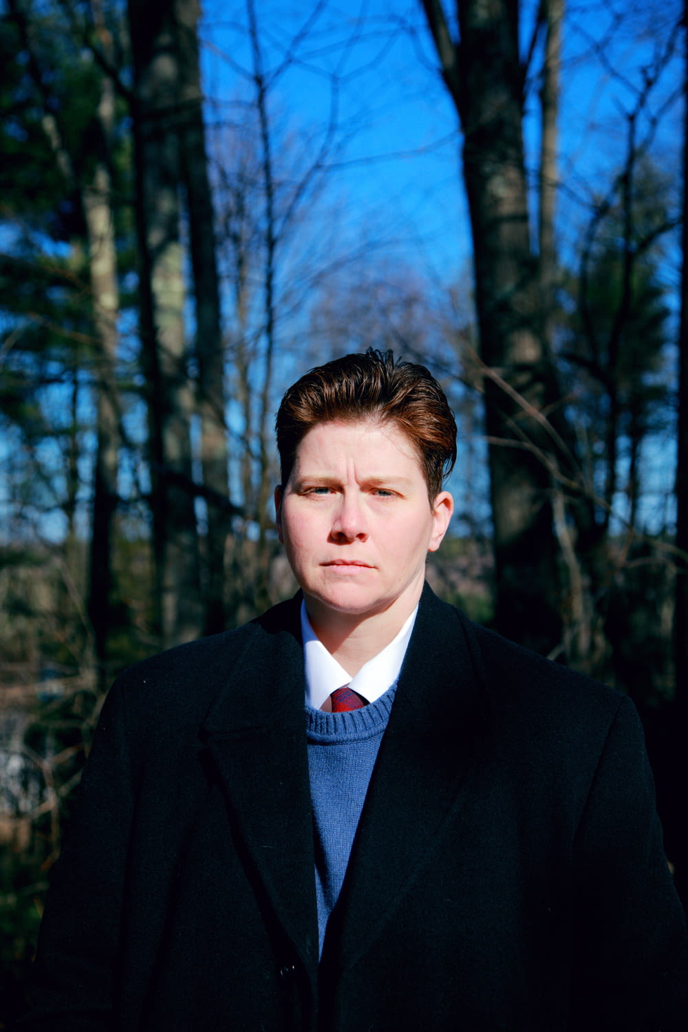 man in black suit jacket standing near trees during daytime
