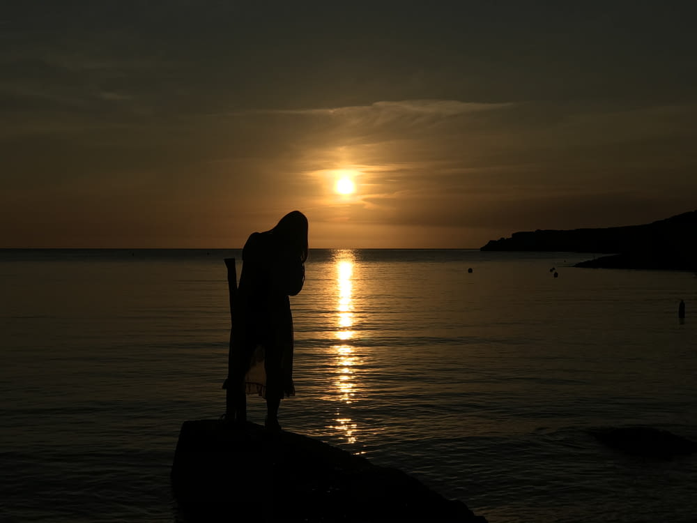 夕暮れ時の水辺の岩の上に立つ女性のシルエット