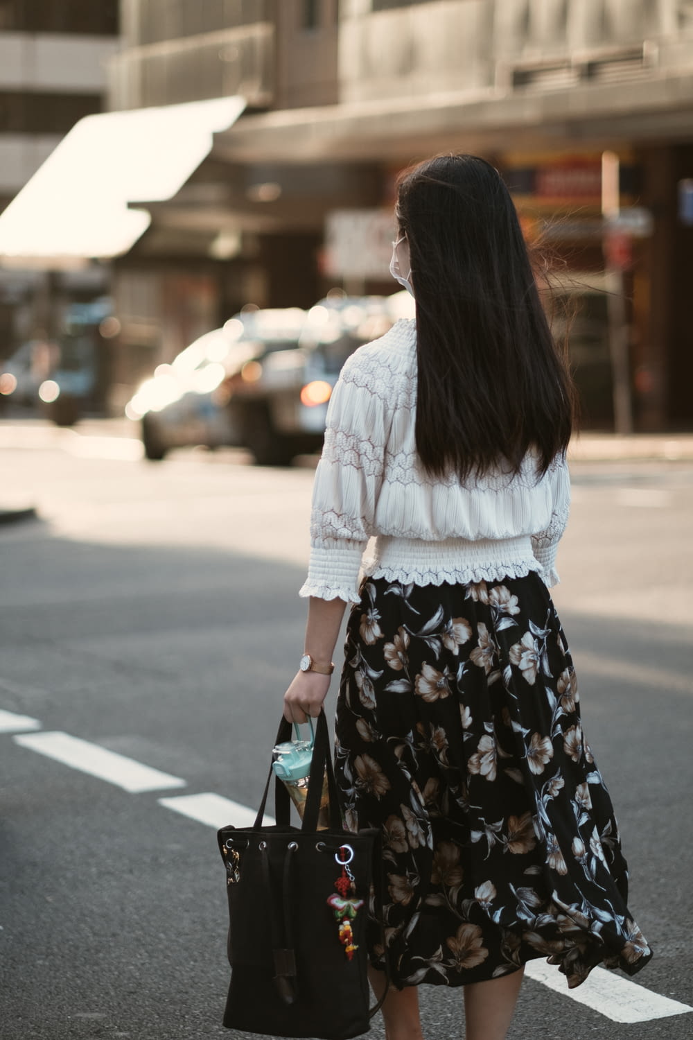 woman in white long sleeve shirt and black floral skirt standing on sidewalk during daytime