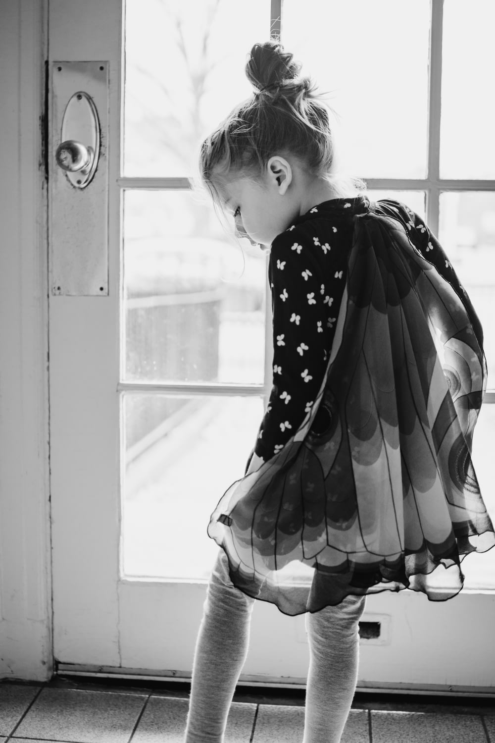 水玉模様のドレスを着た女の子が窓の外を見ているグレースケールの写真