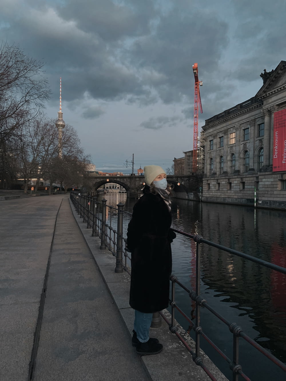 woman in black coat standing on sidewalk near body of water during daytime