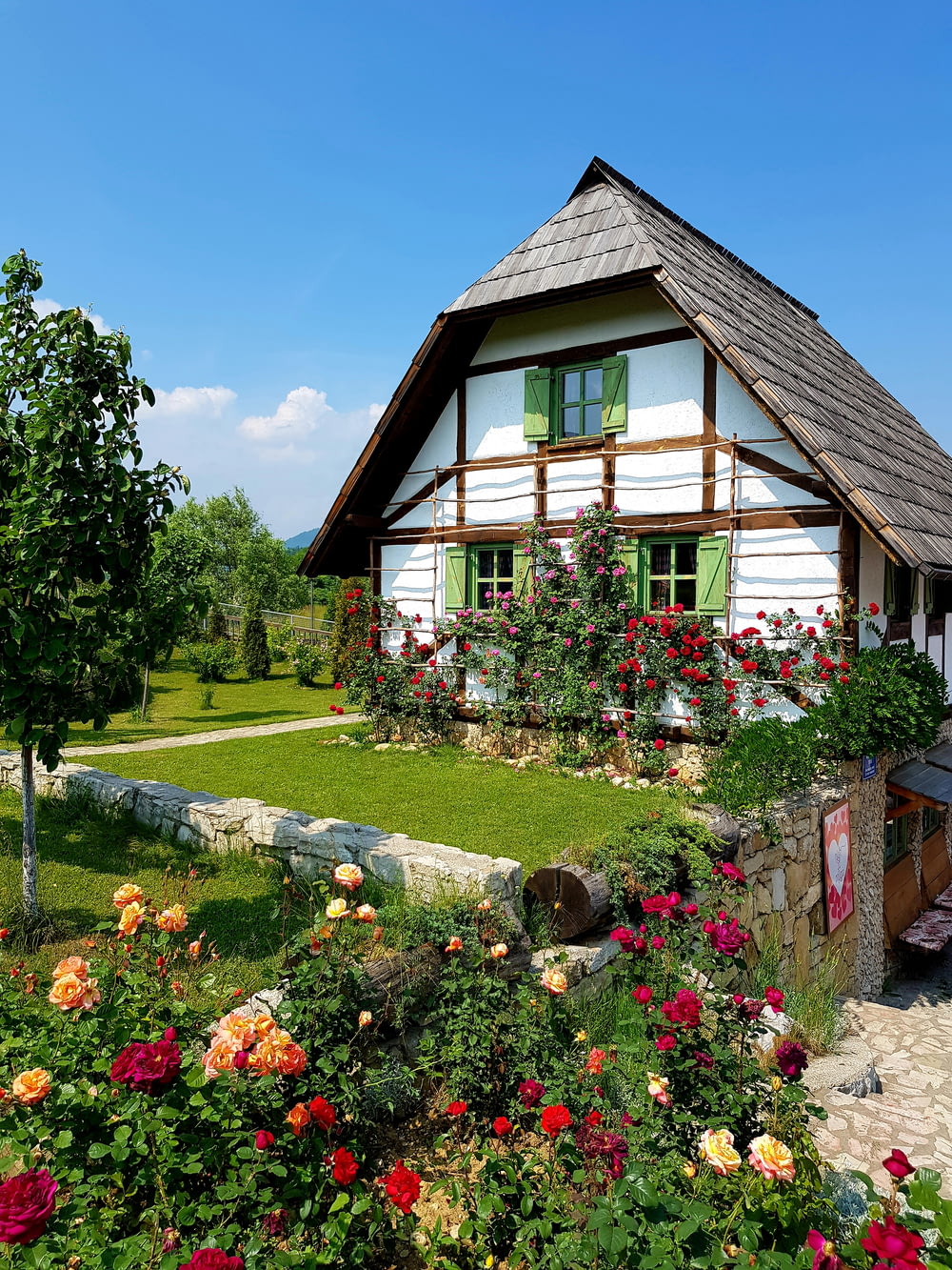 casa di legno marrone circondata da alberi verdi e fiori sotto il cielo blu durante il giorno