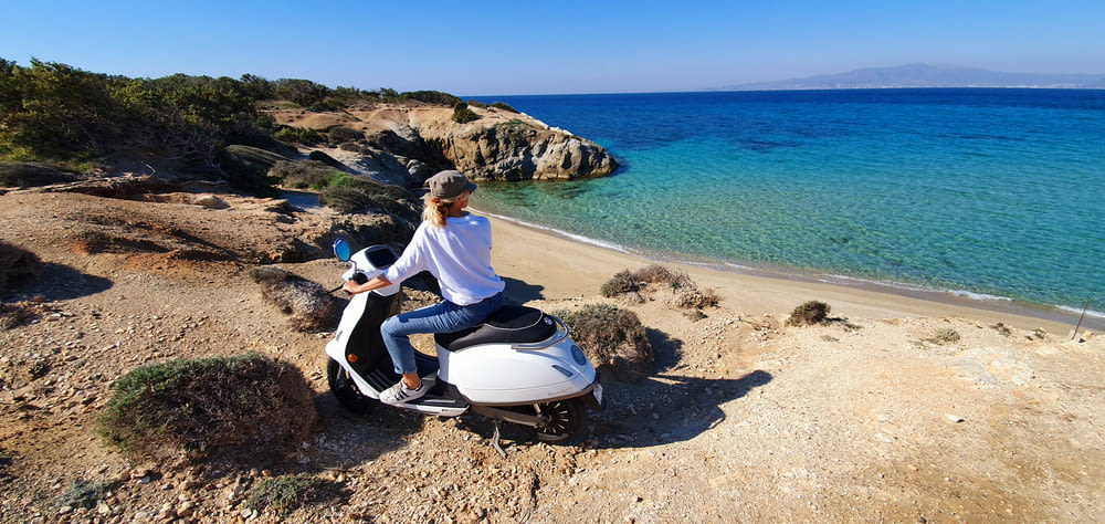 man in white shirt and blue pants sitting on white and black motor scooter on beach