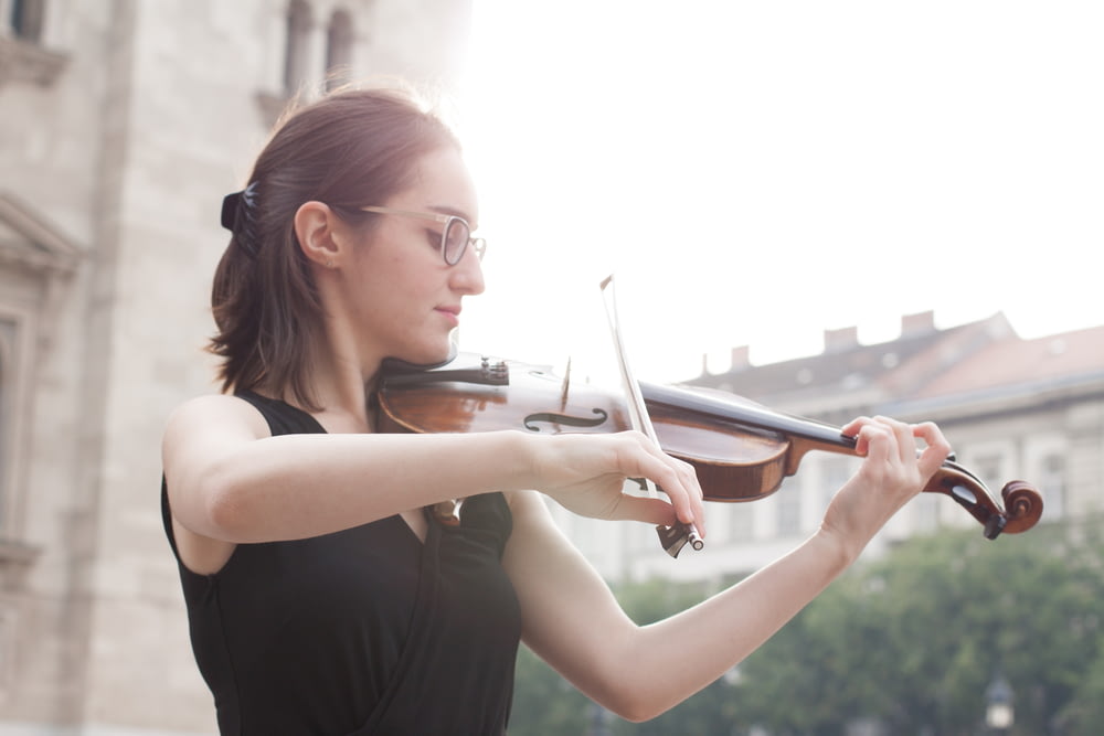Mujer con camiseta negra sin mangas tocando el violín durante el día
