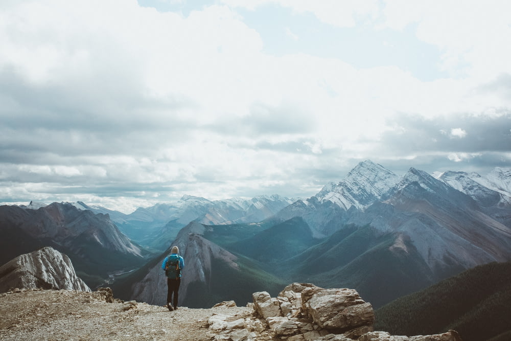 pessoa na jaqueta preta de pé na montanha rochosa durante o dia