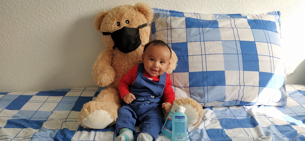 a baby sitting on a bed next to a teddy bear