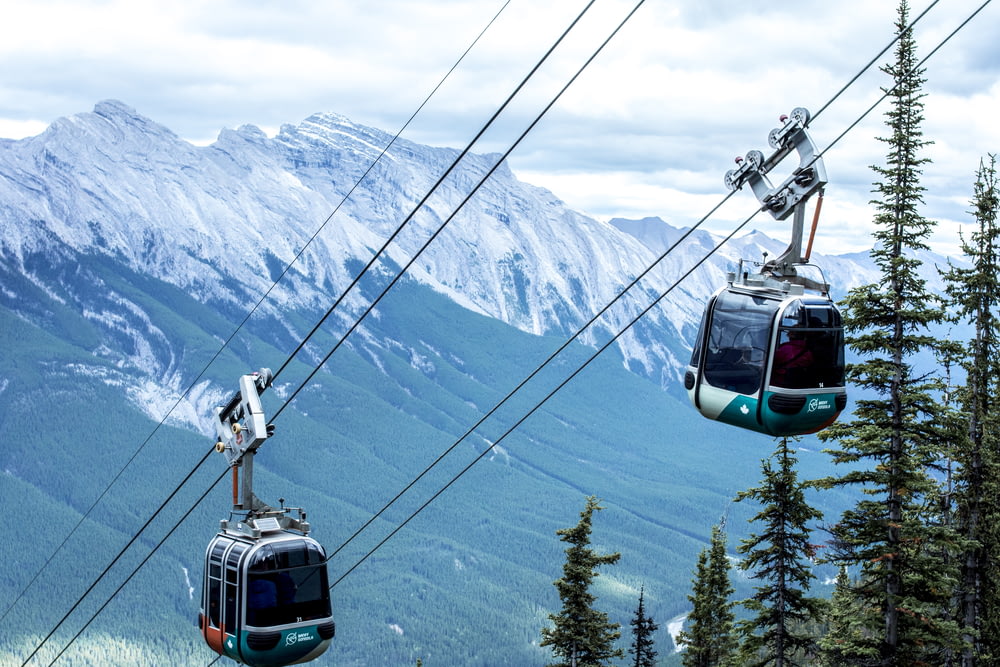 white and black cable car over green pine trees and snow covered mountains during daytime