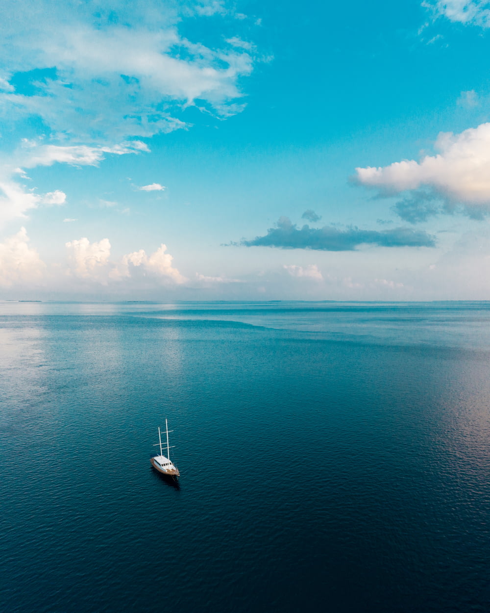 barca bianca sul mare blu sotto il cielo blu e le nuvole bianche durante il giorno